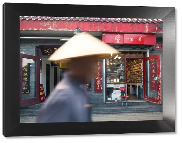 Beijing, China. Old man with conical hat passing in front of a shop in a hutong of