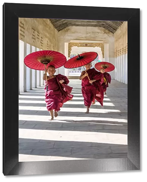 Myanmar, Mandalay division, Bagan. Three novice monks running with red umbrellas in a walkway