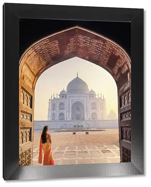 India, a beautiful woman in a red and yellow sari in front of the Taj Mahal at sunrise