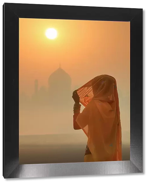 India, woman wearing a traditional sari on a foggy morning with the Taj Mahal in