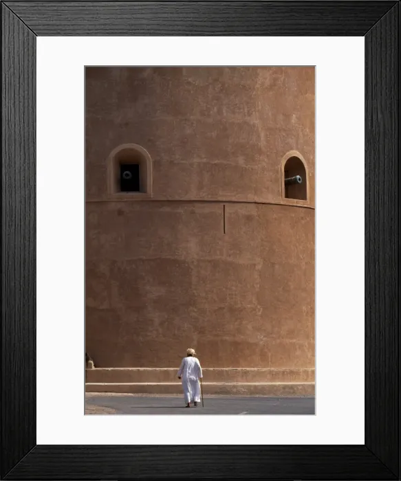 Framed Print : An old Omani man walks beneath the imposing watchtower Framed Print : An old Omani man walks beneath the imposing watchtower