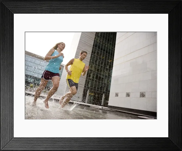 Framed Print : A man and woman running barefoot through water