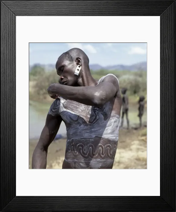 Framed Print : A Mursi man smears his body with a mixture of local Framed Print : A Mursi man smears his body with a mixture of local
