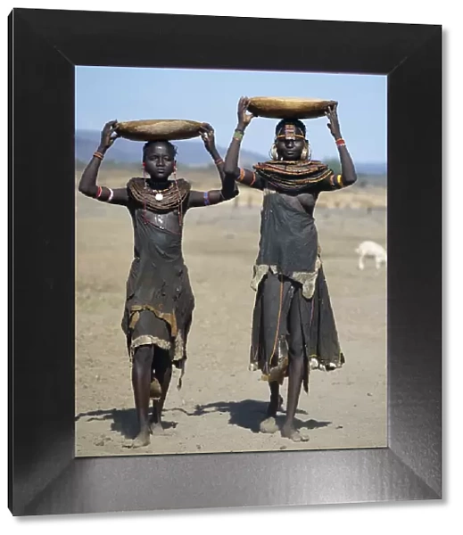 Two Pokot girls carry water in wooden containers on their heads