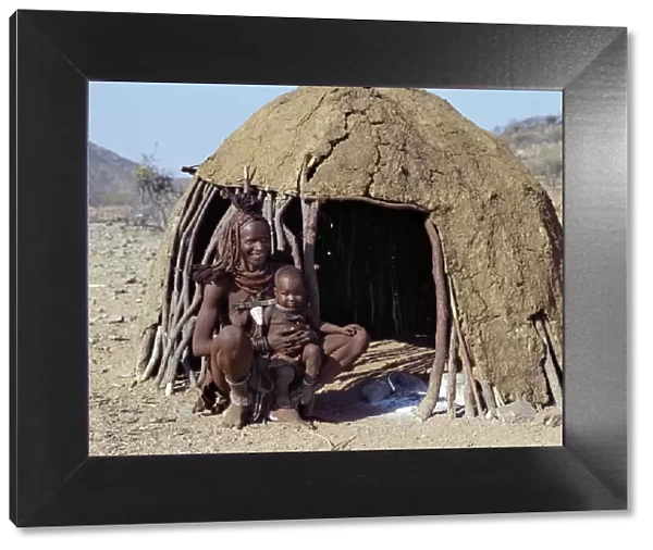 A Himba mother and baby son relax outside their dome-shaped home