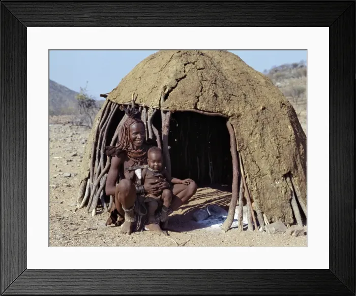 Framed Print : A Himba mother and baby son relax outside their dome-shaped home