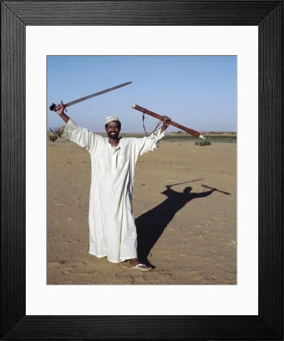 Framed Print : A Nubian man displays his sword at an oasis in Framed Print : A Nubian man displays his sword at an oasis in