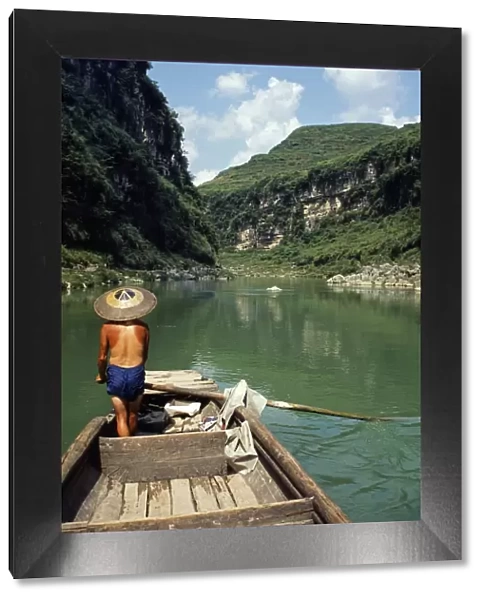A boatman rows between the hills and cliffs of the Chong an River