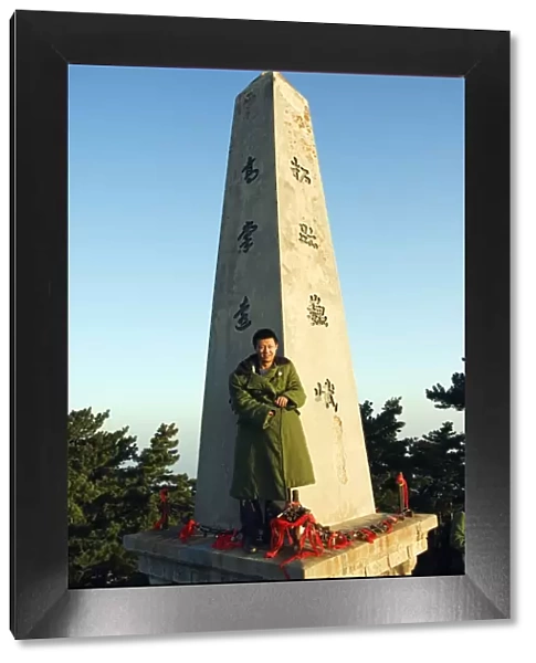A man in green army jacket on a monument on the top of Mount Hua