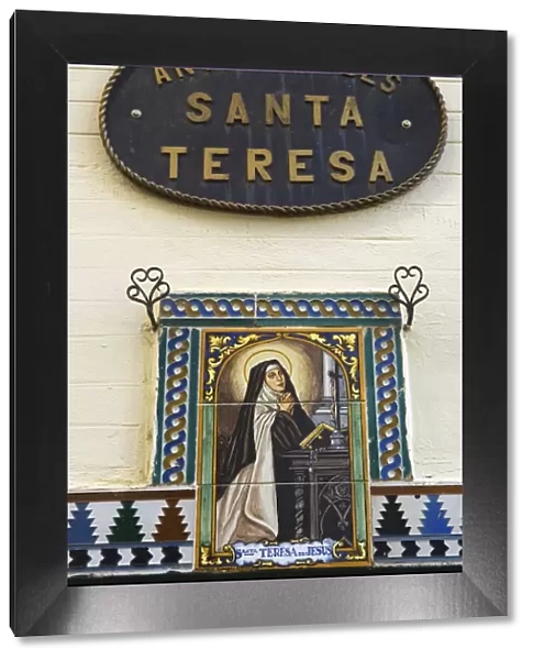 A painted ceramic mural depicting Santa Teresa praying before a cross