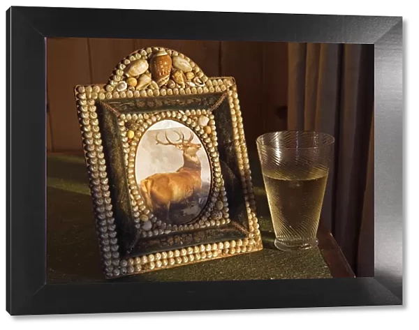 A glass of whisky rests beside a shell encrusted picture