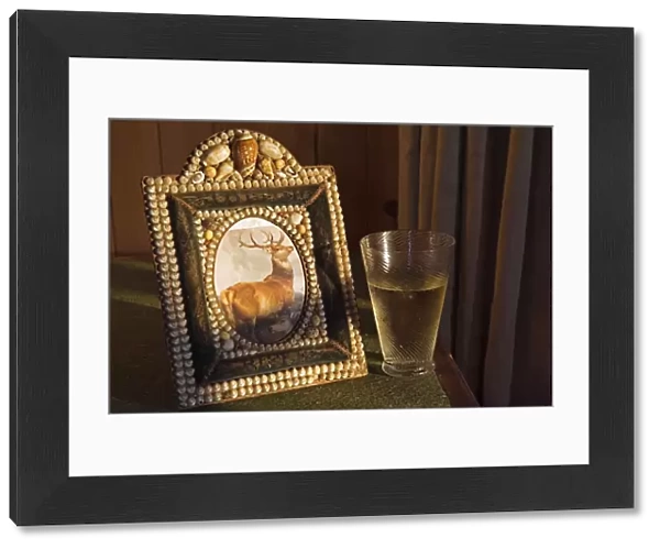 A glass of whisky rests beside a shell encrusted picture