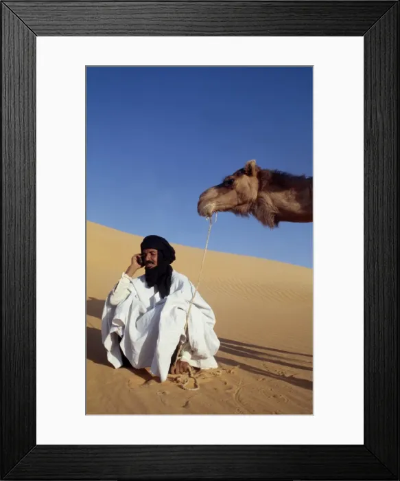 Framed Print : A nomad sits in the desert and talks on his mobile phone Framed Print : A nomad sits in the desert and talks on his mobile phone