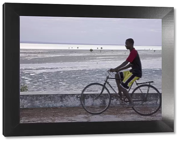 A young man cycling along the sea wall on Ibo Island