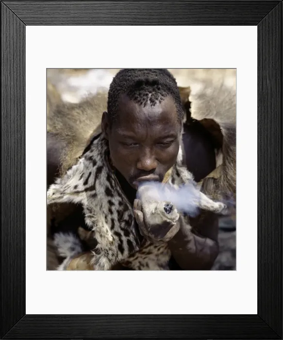 Framed Print : A Hadza hunter smokes cannabis from a crude stone pipe Framed Print : A Hadza hunter smokes cannabis from a crude stone pipe