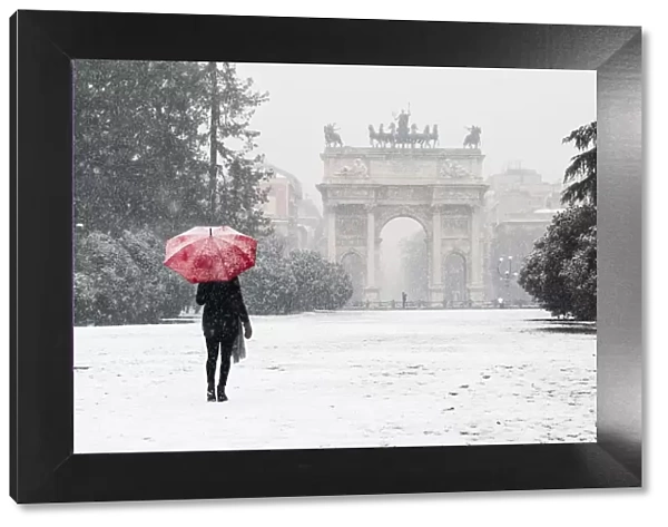 A woman with red umbrella walks in Sempione park during a snowfall. Milan, Lombardy