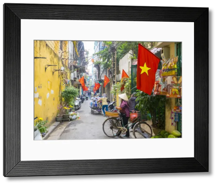 Framed Print : Woman pusing a bicycle through an alleyway lined with red Vietnamese flags, Hoan Framed Print : Woman pusing a bicycle through an alleyway lined with red Vietnamese flags, Hoan
