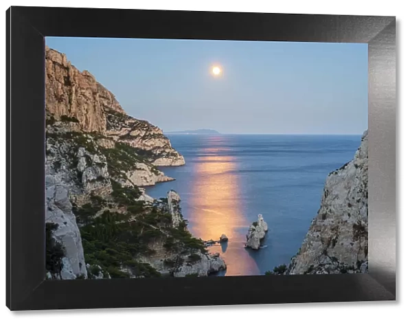Full moon rising over ocean and Mediterranean landscape and Calanque de Sugiton at dusk