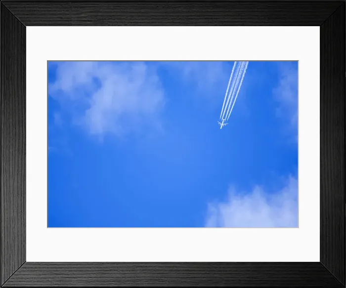Framed Print : An airplane flies across a blue sky leaving vapour trails Framed Print : An airplane flies across a blue sky leaving vapour trails