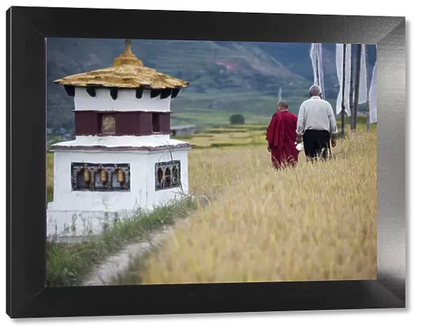 A man and a monk walk past a chorten on the way to the fertility temple in Wangdue