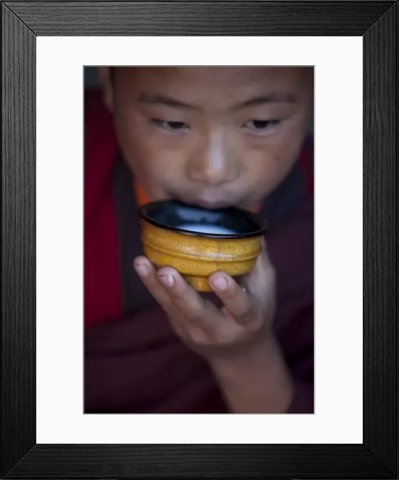 Framed Print : A young monk drinking milk from a wooden bowl in Bhutan