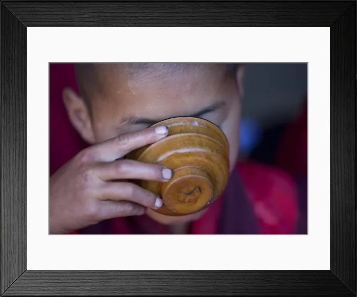 Framed Print : A young monk drinking milk from a wooden bowl in Bhutan