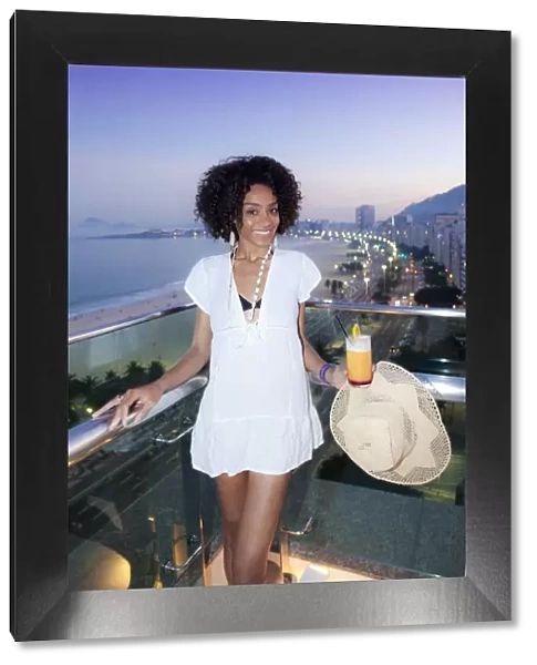 South America, Brazil, Rio de Janeiro, a model with a cocktail stands over Copacabana