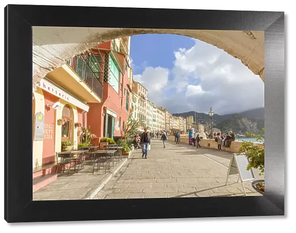 Tourists walking on the picturesque promenade of Camogli framed with an old arch