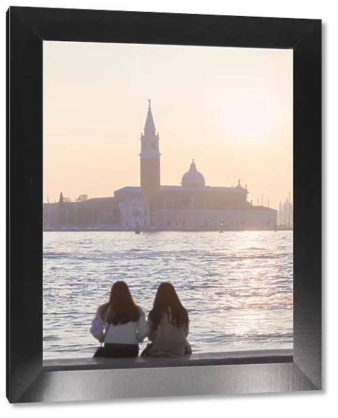 two tourists admire the sunset towards the island of San Giorgio maggiore from the