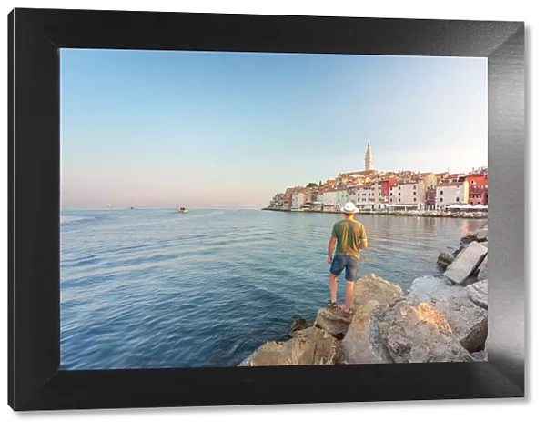 Rovinj - Rovigno, tourist on the rocks of the pier admires the splendid old town, Istria