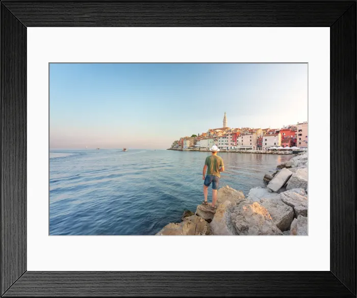 Framed Print : Rovinj - Rovigno, tourist on the rocks of the pier admires the splendid old town, Istria