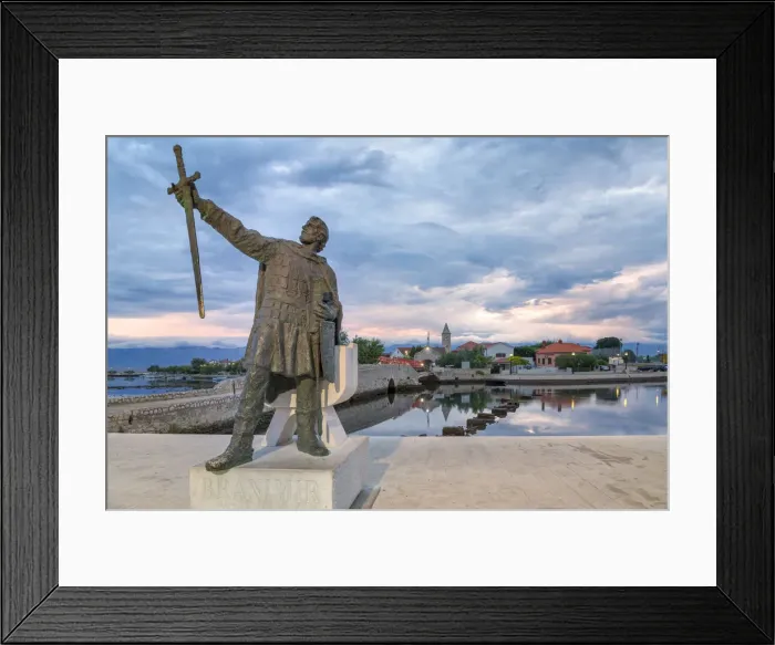 Framed Print : monument of Branimir of Croatia in Nin, on the background the old bridge that connects Framed Print : monument of Branimir of Croatia in Nin, on the background the old bridge that connects