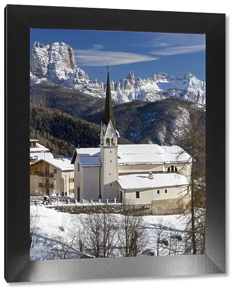 The snowy alpine village and church of Zoppa di Cadore framed by the peak of Bosconero