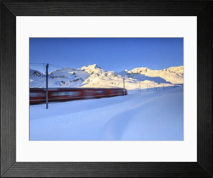 Framed Print : The red train of Bernina whizzes through the snow at the Bernina pass at dawn. Engadine Framed Print : The red train of Bernina whizzes through the snow at the Bernina pass at dawn. Engadine