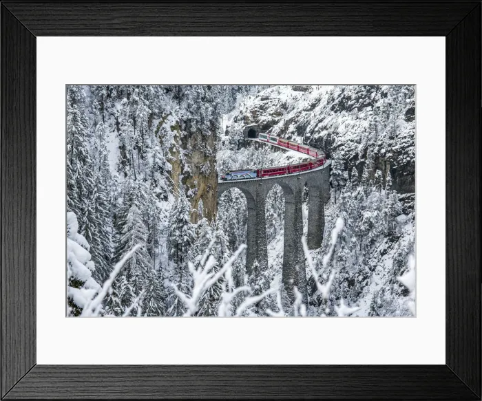 Framed Print : Red train Travelling on the Landawasser Viadukt through the vegetation covered in snow