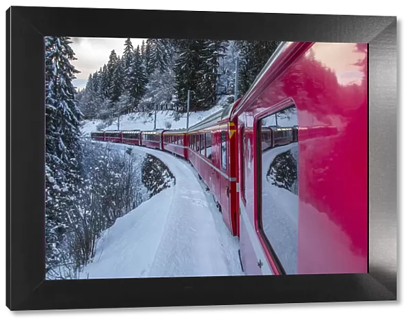 The windows of the red train reflecting the landscape of snowy woods of Sankt Moritz