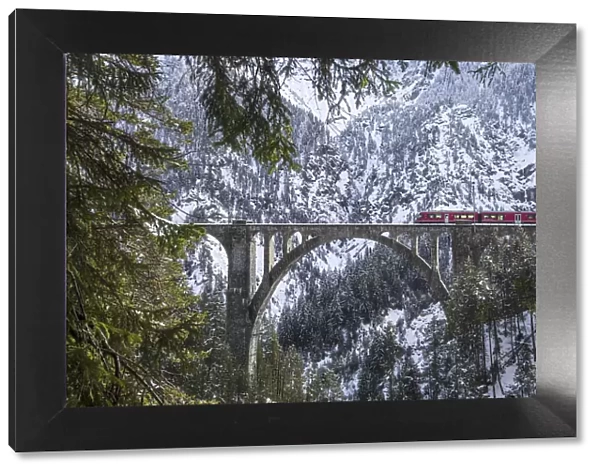 The red train on the Wiesener Viadukt surrounded by snowy mountains