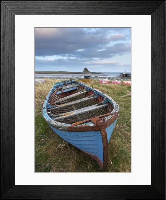 Framed Print : Old fishing boat pulled up on the shore at Holy Island, with the castle across the bay