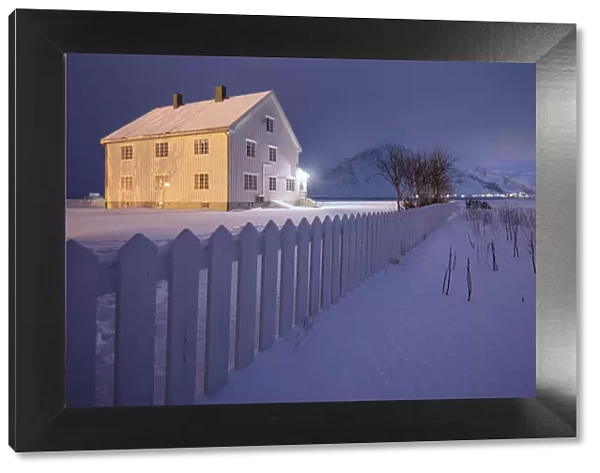 Lights on the typical wooden house surrounded by snow Flakstad Lofoten Islands Northern