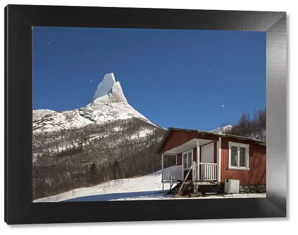 A typical house of fishermen called Rorbu frames the snowy Stetind mountain under