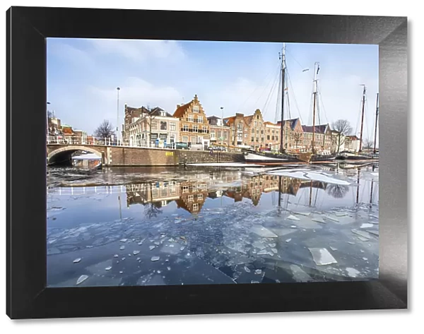 Buildings in Harleem reflecting in the half-frozen Spaarne River, Holland