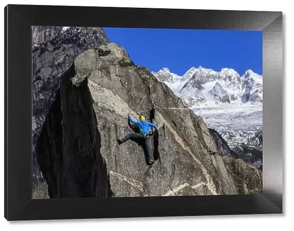 Climber on steep rock face in the background blue sky and snowy peaks of the alps