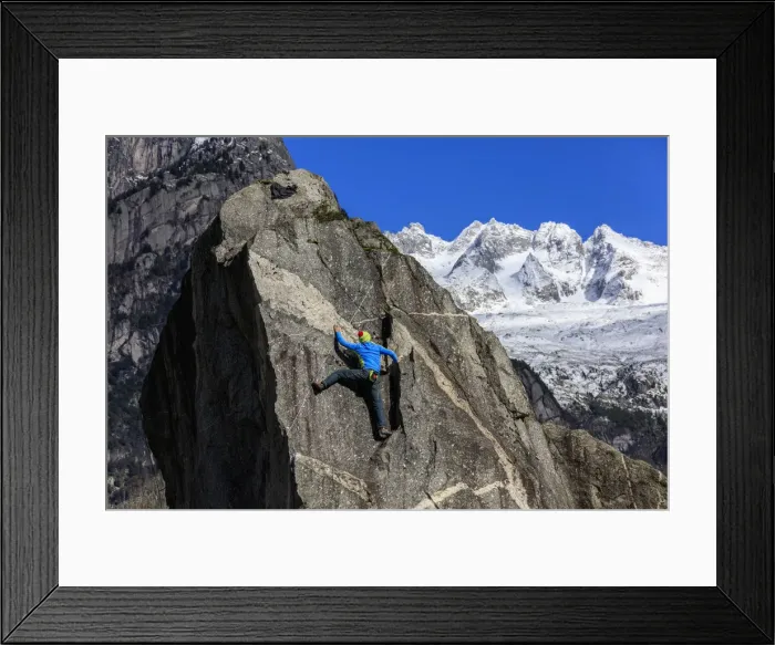 Framed Print : Climber on steep rock face in the background blue sky and snowy peaks of the alps Framed Print : Climber on steep rock face in the background blue sky and snowy peaks of the alps