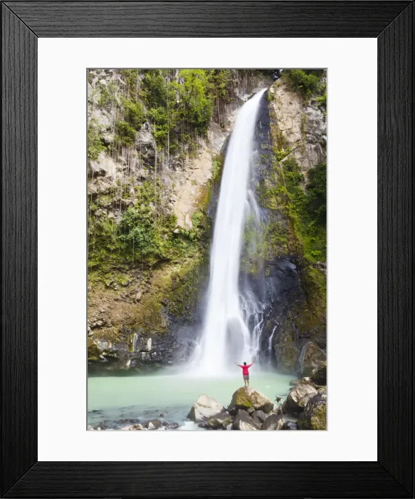 Framed Print : Dominica, Delices. A man stands at the base of Victoria Falls, one of the tallest