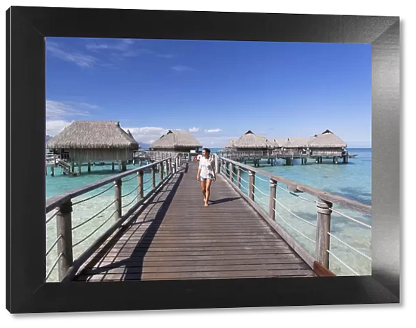 Woman walking on jetty of overwater bungalows of Sofitel Hotel, Moorea, Society Islands