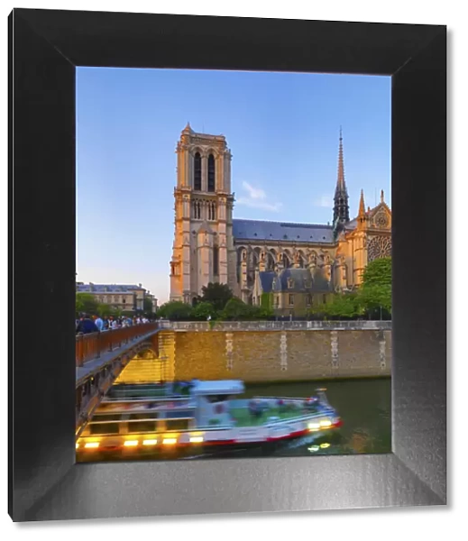 France, Paris, Notre Dame Cathedral and tour boat on River Seine at dusk