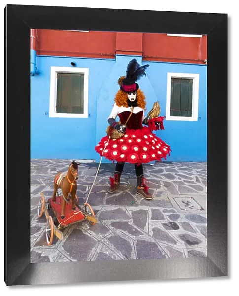 A woman in a colourful costume poses with a toy dog in a street on Burano Island during