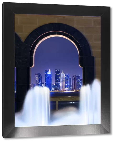 Qatar, Doha. Cityscape at night framed in a arch with fountain in the foreground