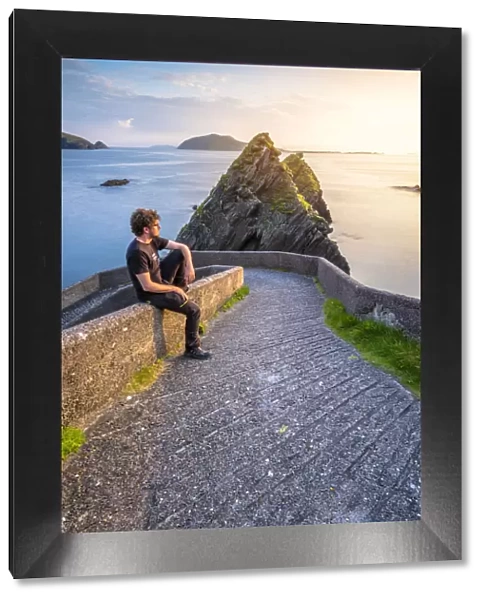 Dunquin pier (Dun Chaoin), Dingle peninsula, County Kerry, Munster province, Ireland, Europe. A man watching the sunset on the trail