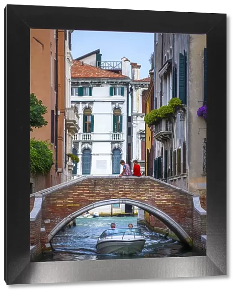 Venice, Veneto, Italy. Two boys sitting on a canals bridge